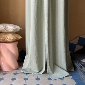 May include: A green and white gingham curtain hangs in a doorway with a pink pedestal and patterned pillows in the foreground. The floor is tiled in a white and blue geometric pattern.