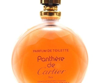 Può includere: Un flacone rotondo di vetro arancione di profumo Panthère de Cartier. Il flacone ha un tappo dorato e un'etichetta che recita "Parfum de Toilette Panthère de Cartier Paris Demonstration/Tester Vente Interdite/Not for Sale 50 ml 1,6 fl. oz."