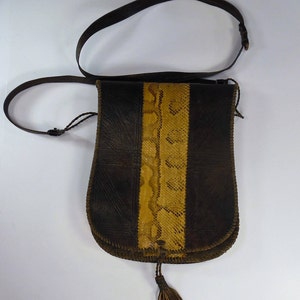 Può includere: Una borsa di pelle marrone con un pannello in pelle di serpente e un pon pon. La borsa ha una lunga tracolla e si chiude con una patta.