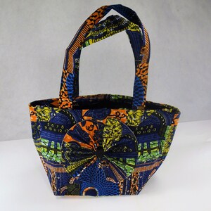 May include: A small, blue, orange, and yellow tote bag with a bow made from the same fabric. The bag has a geometric pattern with numbers on it.