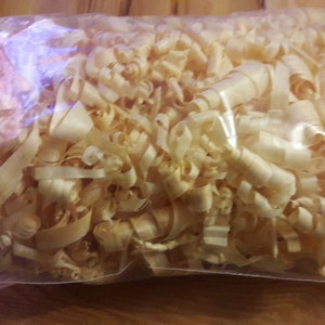 Op de afbeelding: Een doorzichtige plastic zak gevuld met houtsnippers. De snippers zijn lichtbruin en lijken van den of ceder te zijn.