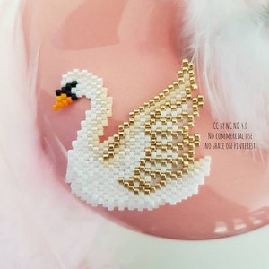 Puede incluir: Un cisne de cuentas blancas y doradas con un diseño detallado. El cisne está sobre un fondo rosa.