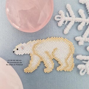 May include: A beaded polar bear figure in white and light yellow, with black eyes and nose, rests on a light blue surface. A pink heart-shaped stone and a white snowflake are also present. The image includes text: CC BY NC ND 4.0, No commercial use, No share on Pinterest.