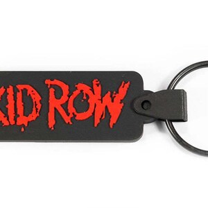 May include: Black rubber keychain with a red "SKID ROW" logo. The keychain has a metal ring.