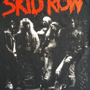 May include: Black and white photo of a rock band, Skid Row, with the band name in red letters above them.