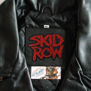 May include: Black leather jacket with a red "Skid Row" patch sewn on the inside of the collar. The patch is on a black background with white stitching. The jacket has a size tag that says "46".