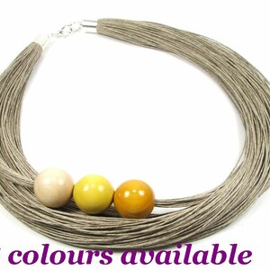 May include: A long, layered linen necklace with a silver clasp and four wooden beads in shades of beige, yellow, and orange.