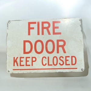 May include: White metal sign with red text that reads "FIRE DOOR KEEP CLOSED".