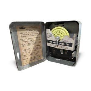 Puede incluir: Interruptor horario Dayton vintage en una caja metálica. La caja abierta revela un dial amarillo, una palanca de encendido/apagado e instrucciones. El texto en la caja dice "HOW TO SET TIME SWITCH".