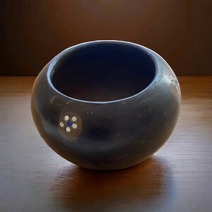 Könnte beinhalten: Eine kleine, schwarze Keramikschüssel mit weißen und blauen Blumenmustern. Die Schüssel ist rund und hat eine glatte, glänzende Oberfläche.