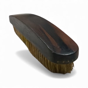May include: A dark brown shoe brush with a curved wooden handle and light brown bristles. The brush is designed for cleaning and polishing footwear. The handle has a smooth, polished finish.