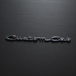 May include: A chrome "Custom Cab" emblem with a cursive font is displayed against a dark wood-grain background. The emblem is slightly angled, and the letters have a subtle, reflective sheen.