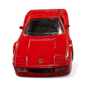 May include: A bright red toy car with a sleek design. The car features a black interior, rectangular headlights, and a small emblem on the front. The toy car is a miniature replica of a classic sports car.