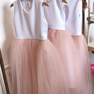 May include: Three white and blush tulle dresses hanging on a rack. The dresses have a white bodice and a blush tulle skirt. The text "Our white & blush" is visible at the top of the image.