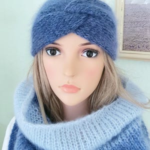 May include: A blue knitted headband and cowl scarf set. The headband has a twisted design, and the scarf is a cowl style. The set is made of a soft, fuzzy material. The colour is a gradient of light to dark blue.