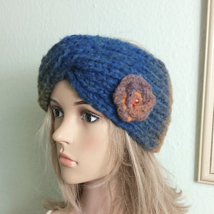 May include: A blue knitted headband with a brown and orange felt flower accent. The headband is twisted and has a soft, textured look.