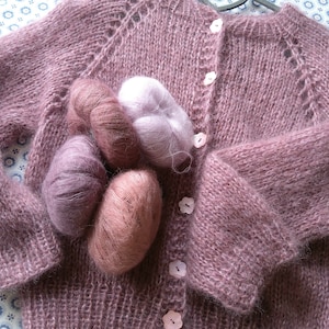 May include: A soft, pink knitted cardigan with a button closure and a delicate openwork pattern. The cardigan is made with a fluffy yarn and has a relaxed fit.