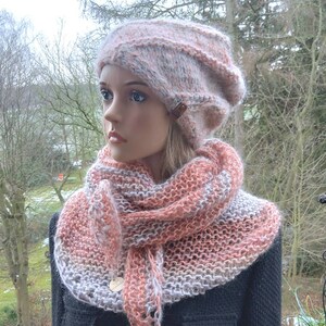 May include: A pink and white knitted hat and scarf set. The hat is a slouchy beanie style and the scarf is a triangular shawl.