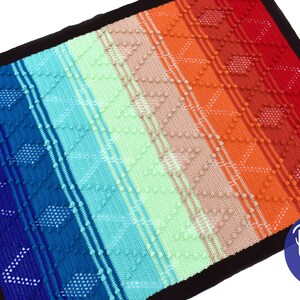 Op de afbeelding: Een kleurrijk regenboog gehaakt deken met een zwarte rand. Het deken is gemaakt met een textuur steek en heeft een herhalend patroon van ruiten. Het deken is gemaakt met een verscheidenheid aan kleuren, waaronder blauw, groen, oranje en rood. Het deken is gelabeld "Dolly Plum".