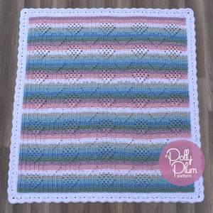 May include: A crochet baby blanket with a white border and a heart pattern in shades of pink, blue, and green. The blanket has a scalloped edge and the text "a Polly Plum pattern" is in the lower right corner.
