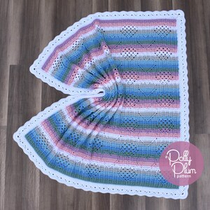 May include: A crocheted baby blanket with a white border and a striped pattern in shades of pink, blue, and green. The blanket is folded in half and has a "a Dolly Plum pattern" label in the bottom right corner.
