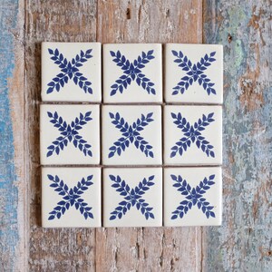 May include: Nine white ceramic tiles with a blue floral design. Each tile features a stylised floral pattern with four leaves arranged in a cross shape.
