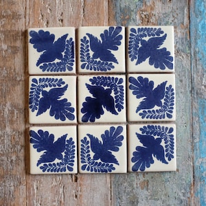 May include: Nine white ceramic tiles with a blue and white floral design. Each tile features a stylised bird with a floral pattern around it.