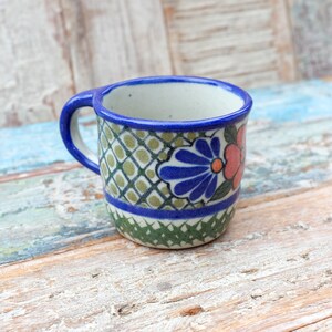May include: A small, blue and green ceramic mug with a floral design. The mug has a white interior and a blue rim.
