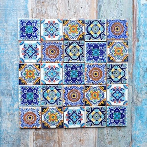 May include: A collection of twenty-five square ceramic tiles arranged in a five-by-five grid. Each tile features a unique, intricate geometric and floral pattern in vibrant shades of blue, yellow, orange, and white, creating a colourful mosaic display.