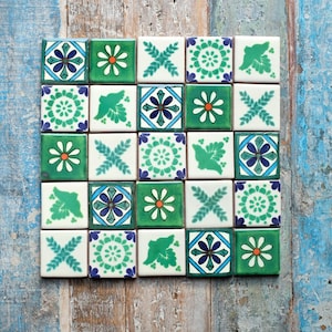 May include: A square arrangement of twenty-five ceramic tiles featuring five repeating patterns in shades of green, white, and blue. The designs include stylised flowers, geometric floral medallions, leafy sprigs, and bird silhouettes on a white background.