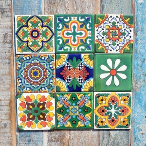 May include: A collection of nine square ceramic tiles arranged in a three-by-three grid. Each tile features a distinct, colourful geometric or floral pattern in shades of green, yellow, orange, blue, and white, with intricate symmetrical designs.