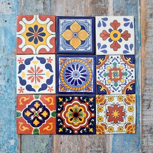 May include: A collection of nine square ceramic tiles arranged in a three-by-three grid. Each tile features a distinct, colourful geometric and floral pattern in shades of blue, yellow, red, orange, green, and white, with intricate symmetrical designs.