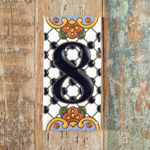 May include: Rectangular ceramic tile with the number 8 in navy blue. The tile has a white background with a black dot grid pattern. Decorative floral elements in orange, yellow, and green adorn the top and bottom.