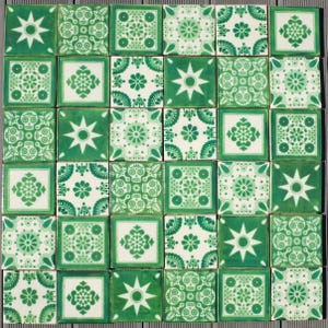 May include: A collection of square ceramic tiles with a green and white floral and geometric pattern. The tiles feature various designs, including starbursts, flowers, and stylized skulls. The tiles are arranged in a grid pattern.