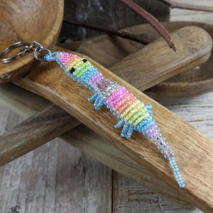 May include: A colourful beaded keychain shaped like a shrimp. The shrimp is made with rainbow coloured beads and has a silver key ring.