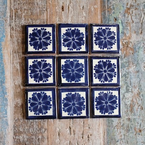 May include: Nine blue and white ceramic tiles with a floral design. Each tile features a stylised flower with a blue centre and white petals.