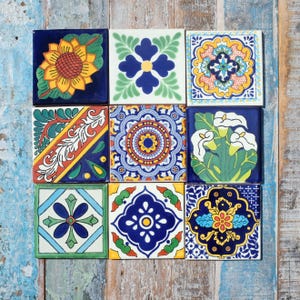 May include: A collection of nine square ceramic tiles arranged in a three-by-three grid. Each tile features distinct hand-painted patterns including a yellow sunflower, white calla lilies, geometric floral motifs, and intricate blue and yellow mandalas.