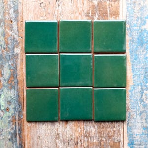 May include: Nine square, emerald green tiles arranged in a 3x3 grid. The tiles have a glossy finish and are set against a backdrop of weathered, multi-coloured wooden planks. The tiles are a vibrant, solid colour.