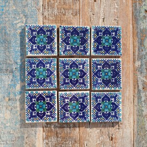 May include: Nine blue and white ceramic tiles with a floral pattern. The tiles have a blue background with white flowers and yellow accents.
