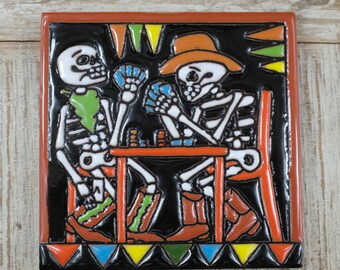 May include: Two skeletons wearing hats and boots play cards at a table with a red and orange border. The background is black with colorful triangles and a red and orange border.