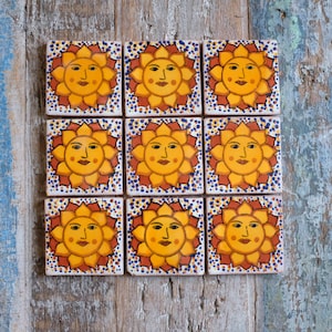 May include: Nine ceramic tiles featuring a yellow sun design. Each tile depicts a smiling sun face with red cheeks against a yellow background. The tiles are bordered with a blue and white pattern and small white dots.