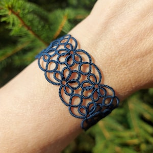 May include: A navy blue crocheted bracelet with a delicate floral pattern.