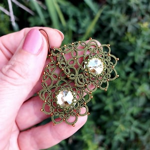 Puede incluir: Pendientes de cuentas verdes y doradas con un gran cristal en el centro de cada pendiente.