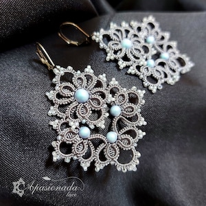 May include: A pair of silver earrings with a delicate lace design and light blue beads. The earrings are in the shape of a flower and are hanging from silver hooks.