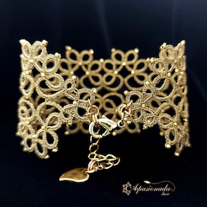 Puede incluir: Un brazalete dorado hecho de encaje de ganchillo delicado con un dije en forma de corazón y un cierre de broche.