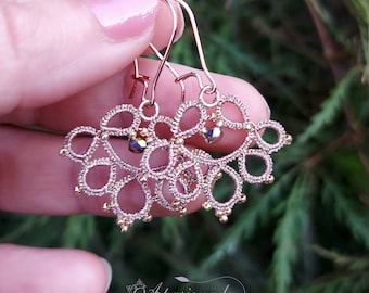 May include: Rose gold earrings with delicate lacework and iridescent beads. The earrings are handmade and feature a unique design.