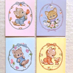 May include: Four rectangular greeting cards featuring illustrations of kittens in oval frames. The top left is pink with a kitten in a blue sweater. The top right is lavender with a kitten and flowers. The bottom left is blue with a kitten. The bottom right is yellow with a kitten and a mouse.