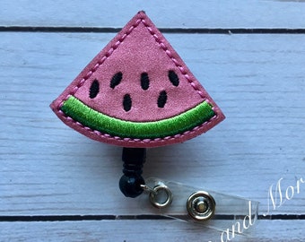 May include: A pink watermelon slice felt badge reel with black seeds and a green rind. The badge reel has a black retractable cord and a clear plastic clip.