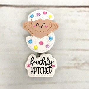 This listing is for baby in an egg with freshly hatched Badge Reel. The badge reel is made with a baby hatching egg feltie stitched on white glitter vinyl backed with felt The freshly hatched word feltie is on white glitter vinyl is backed with felt