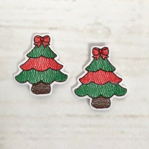 Könnte beinhalten: Zwei gestickte Weihnachtsbaum-Patches. Jeder Baum hat grüne und rote Schichten, eine rote Schleife oben und einen braunen Stamm. Die Patches befinden sich auf einer weißen Holzoberfläche.